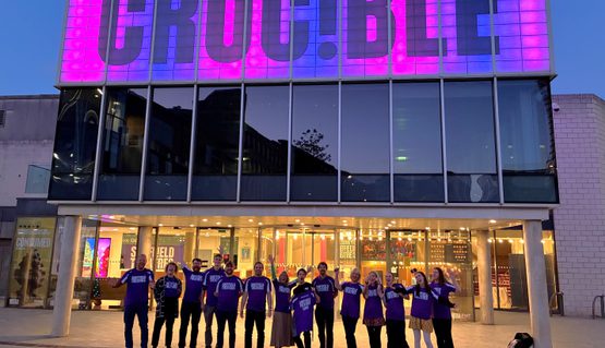 A group of people wearing purple running t shirt line up in front of the Crucible Theatre.