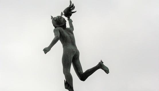 A statue of the Roman messenger god Mercury, taken from below as it stands at the top of a building.