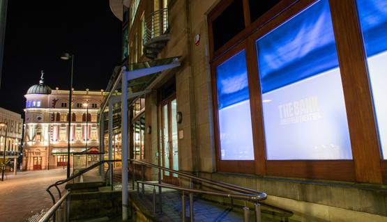 The exterior of The Bank, a space owned by Sheffield Theatres for talent development. Across the square the Lyceum can be seen, lit up for the night.