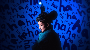 Julia Masli standing in front of a wall. The wall features the following text: 'ha ha ha ha ha ha ha'.