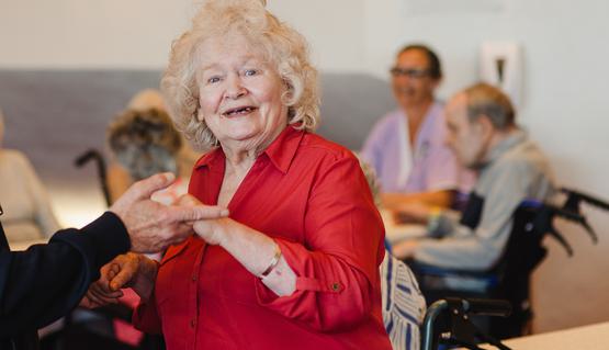 A Dementia Friendly Tea Dance at Sheffield Theatres. Photo by Becky Payne. An older woman holds someone’s hands as she dances. She has a big smile on her face.