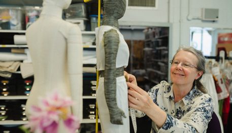 A person smiles as they adjust clothing on a mannequin.