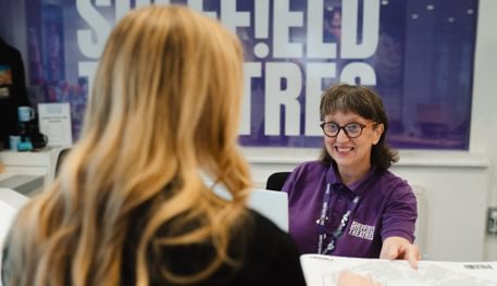 A person smiles as they serve a customer behind Sheffield Theatres' Box Office