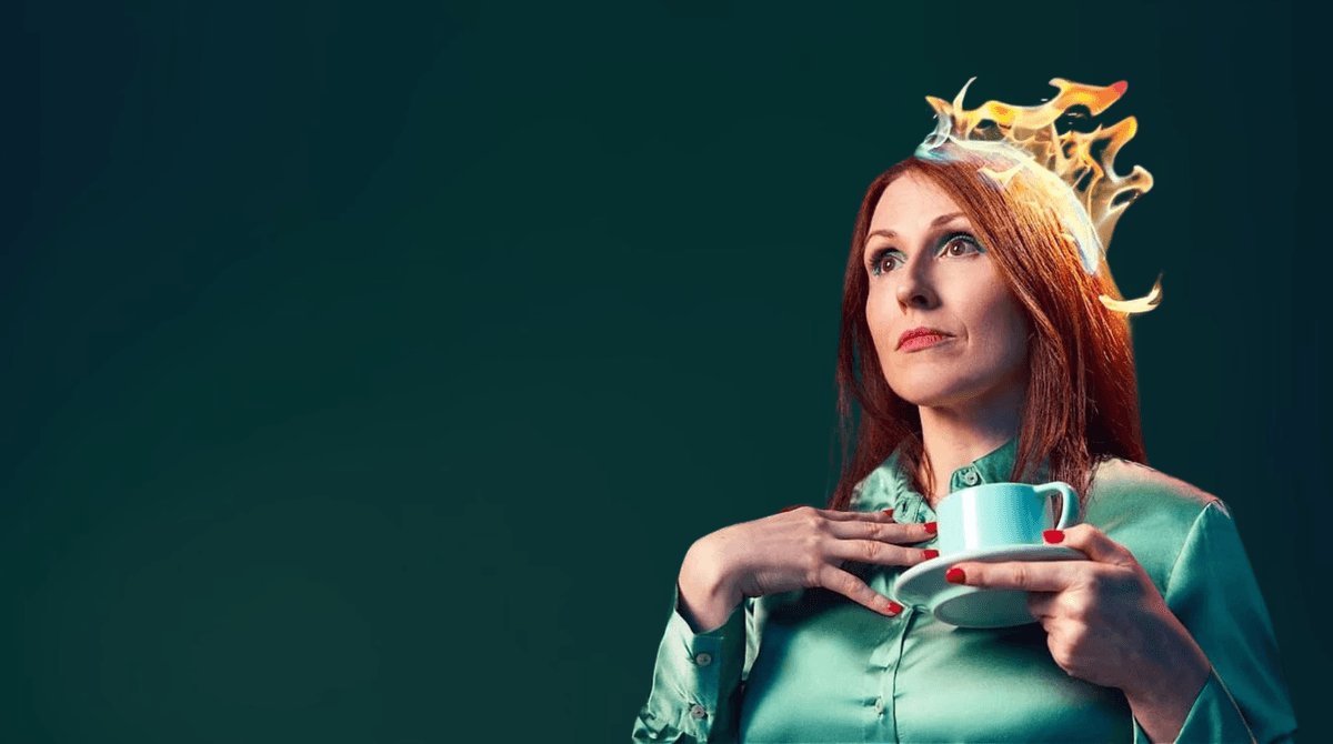 An image of Suzy Crothers, a white woman with ginger hair, holding a tea cup. Her hair is on fire and she is looking to the side.